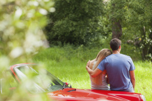 Loving couple admiring nature while leaning on their cabriolet on a sunny day